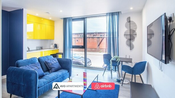 Ein modernes Apartment mit einem blauen Sofa, einem Esstisch und einer Küche mit gelben Schränken.