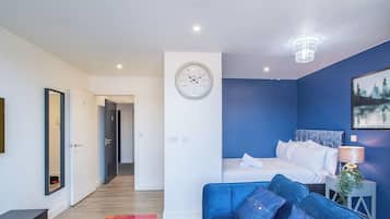 A modern bedroom with a bed, a blue couch, a chandelier, and a clock on the wall.