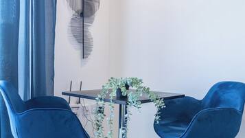 A modern living room with a dark wooden table, two blue chairs, a potted plant, and a decorative wall piece.