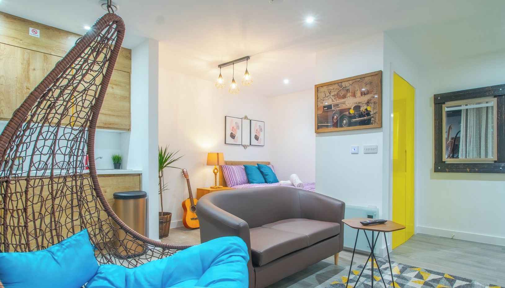 Ein modernes Wohnzimmer mit Hängesessel, Sofa und einem kleinen Tisch. Eine Gitarre, eine Lampe und ein Gemälde sind an der Wand zu sehen.