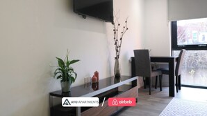Ein modernes Wohnzimmer mit einem an der Wand montierten Flachbildfernseher, einem Essbereich mit Tisch und Stühlen sowie einer Zimmerpflanze auf einer Konsole.
