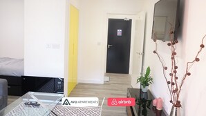 Eine moderne Wohnung mit Bett, Sofa, Glastisch, Fernseher und einer Tür mit einem Schild.