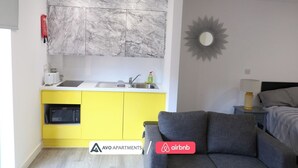 Ein kompakter Wohnraum mit Küchenzeile, einer Marmor-Spritzschutzleiste, einem gelben Schrank und einem grauen Sofa.