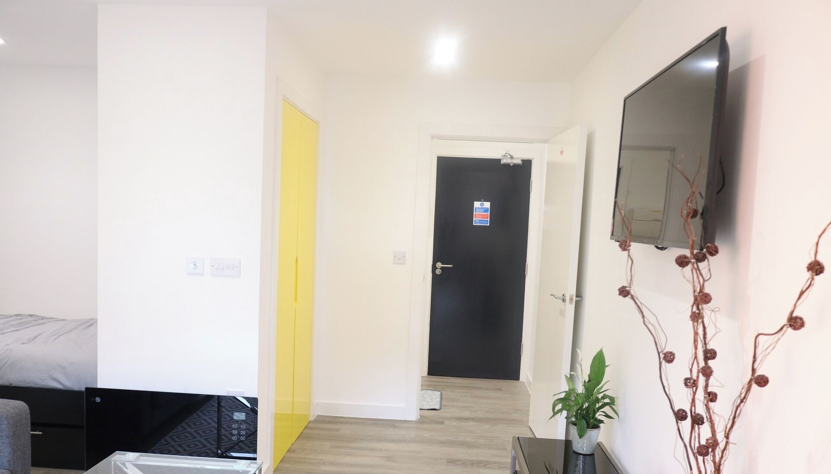 A modern apartment with a bed, a sofa, a glass coffee table, a TV, and a door with a sign.