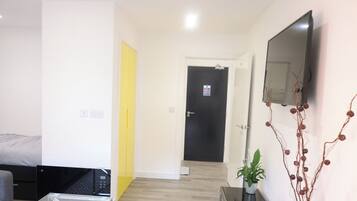 A modern apartment with a bed, a sofa, a glass coffee table, a TV, and a door with a sign.