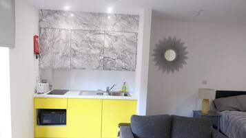 A compact living space with a kitchen area featuring a marble backsplash, a yellow cabinet, and a grey sofa.