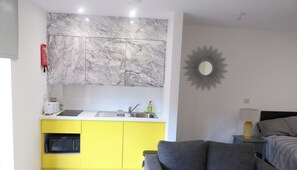 A compact living space with a kitchen area featuring a marble backsplash, a yellow cabinet, and a grey sofa.
