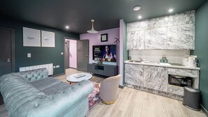 A modern bedroom with a large bed, a small sofa, a TV, and a kitchen area with marble countertops. - Boutique Studio with Designer Finishes – APT 16 (South Yorkshire)