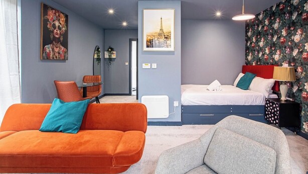 A modern hotel room with a blue accent wall, a bed with white bedding, a grey armchair, an orange sofa, and a red headboard. - Lovely Studio Sheffield Centre – APT 11 (Sheffield)