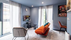 A modern living room with a large window, a flat-screen TV, a sofa, and a chair. - Lovely Studio Sheffield Centre – APT 11 (Sheffield)