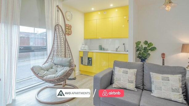Un apartamento moderno con un sillón colgante, un sofá, una cocina con armarios amarillos y un reloj visible.