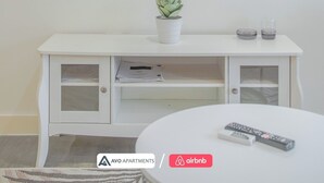 Un mueble blanco para televisor con una planta en maceta, dos controles remotos y un pequeño recipiente de vidrio.