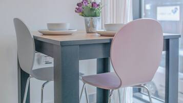 A modern dining area with a table and chairs, a vase with flowers, and a view of the street outside.