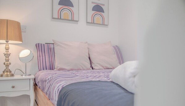 A bedroom with a bed, a bedside table with a lamp, and two framed artworks on the wall.