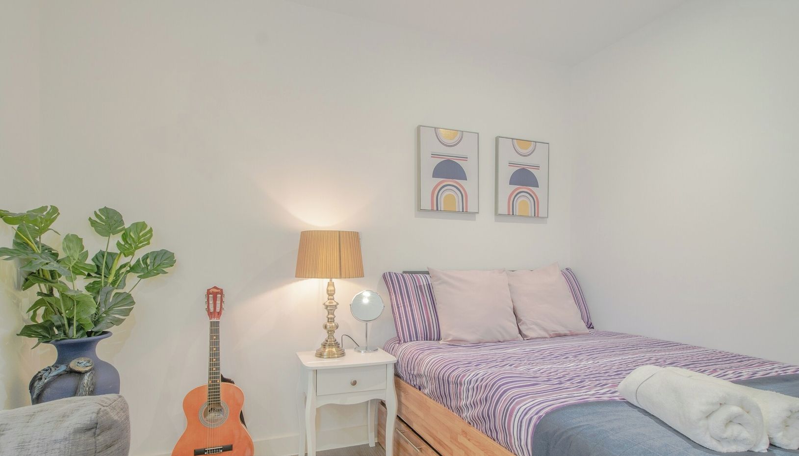 Ein Schlafzimmer mit einem Bett, einer Gitarre, einer Lampe und einer Pflanze.