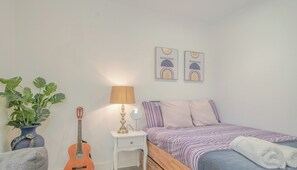 A bedroom with a bed, a guitar, a lamp, and a plant.
