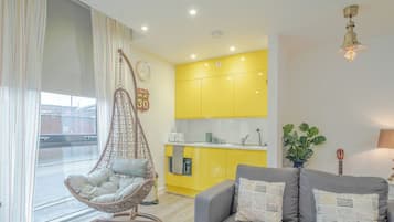 A modern apartment with a hanging chair, a sofa, a kitchen with yellow cabinets, and a visible clock.
