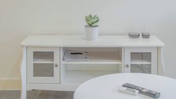 A white TV stand with a potted plant, two remote controls, and a small glass container.