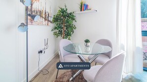Una sala de estar moderna con una mesa de vidrio, dos sillas, una planta en maceta y una pintura de un paisaje urbano en la pared.