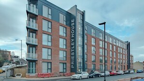 Un edificio moderno de varios pisos con un cartel llamativo que dice "Priestley House".