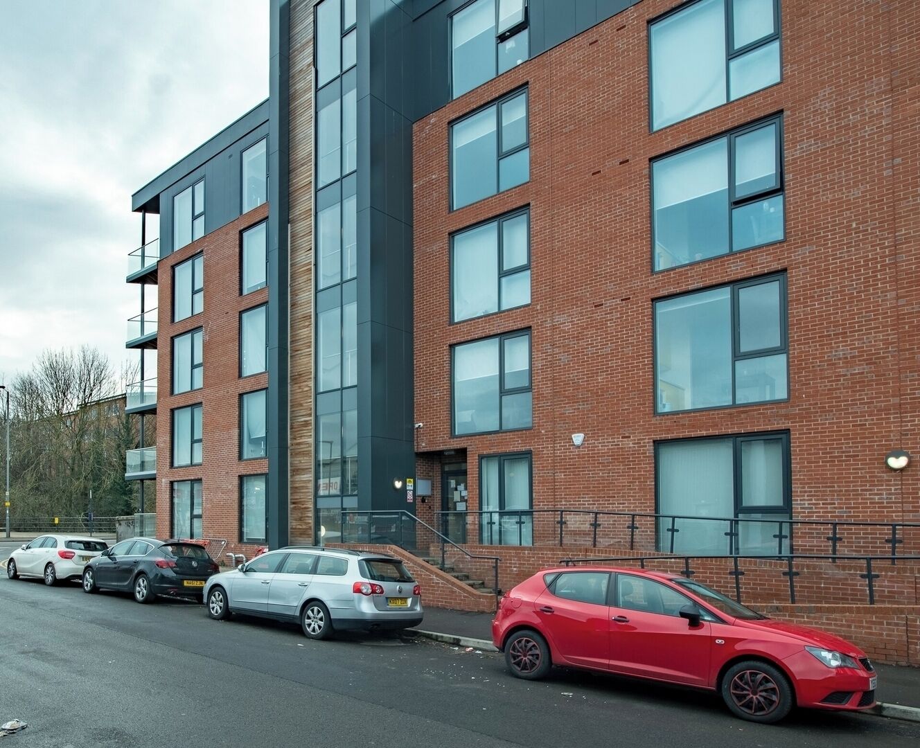 A multi-story building with a brick facade and large windows. There are several cars parked in front.