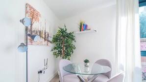 Un soggiorno moderno con un tavolo in vetro, due poltrone, una pianta in vaso e un dipinto con una veduta urbana.