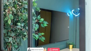 Un salon moderne avec un grand téléviseur à écran plat, une plante en pot et un luminaire circulaire bleu.