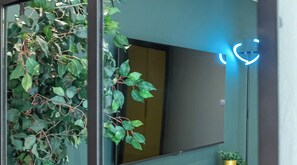 Una sala de estar moderna con un televisor de pantalla plana grande, una planta en maceta y una lámpara circular azul.