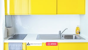 Une cuisine avec des meubles de couleur jaune, un évier, un grille-pain et une bouteille de liquide vaisselle.