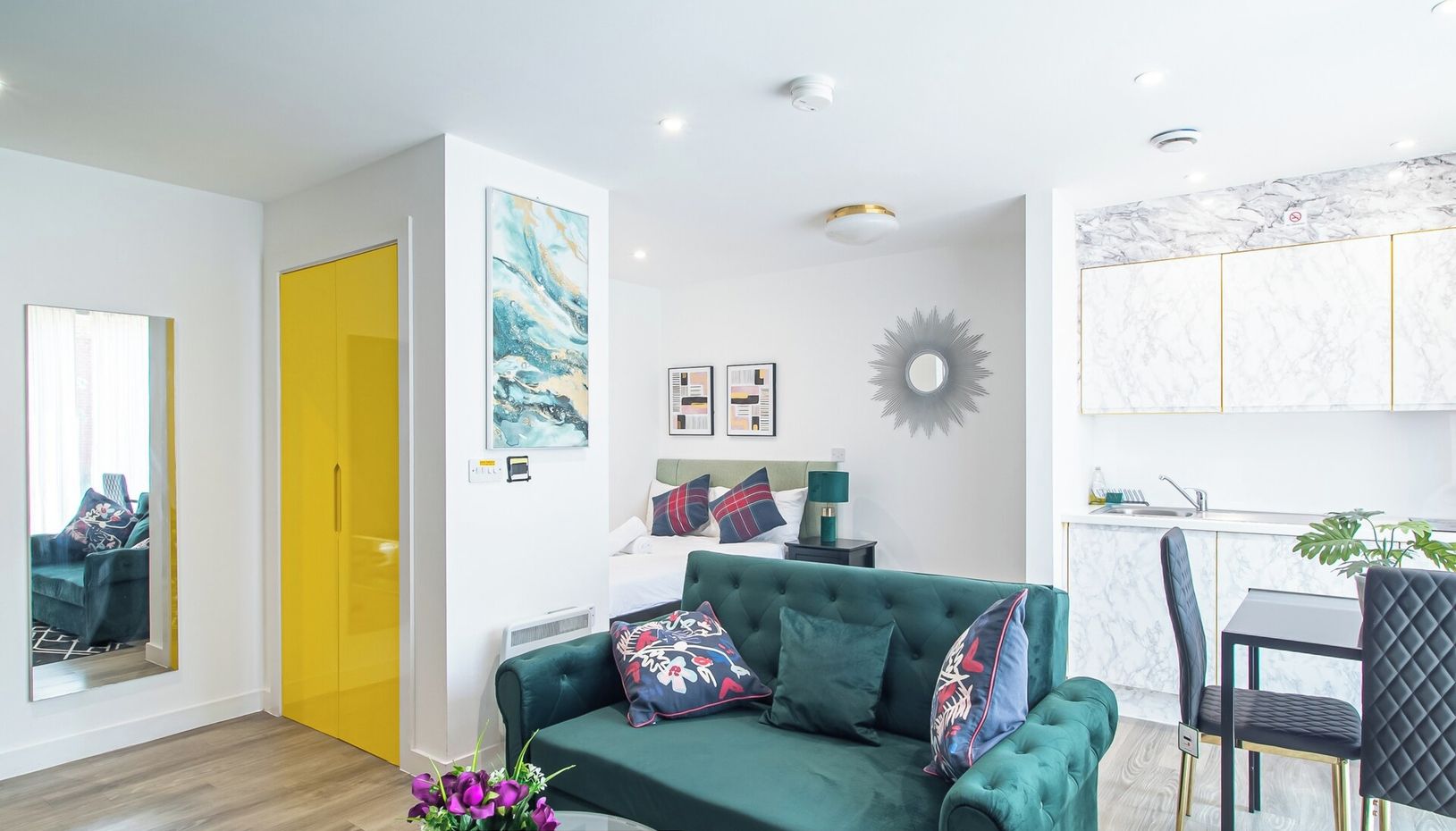 Een moderne woonkamer met een groene bank, een eettafel en een keukenhoek.