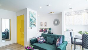 A modern living room with a green sofa, a dining table, and a kitchen area. - Urban Studio Perfect for City Explorers – APT 20 (South Yorkshire)