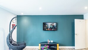 A modern living room with a teal accent wall, a mounted TV, a black coffee table with a vase of flowers, and a unique hanging chair. - Urban Studio Perfect for City Explorers – APT 20 (South Yorkshire)