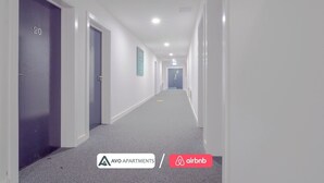 A hallway with doors labeled with numbers, a carpeted floor, and a sign for AVO APARTMENTS. - Creative Studio With Rustic Charm – APT 22 (Sheffield)