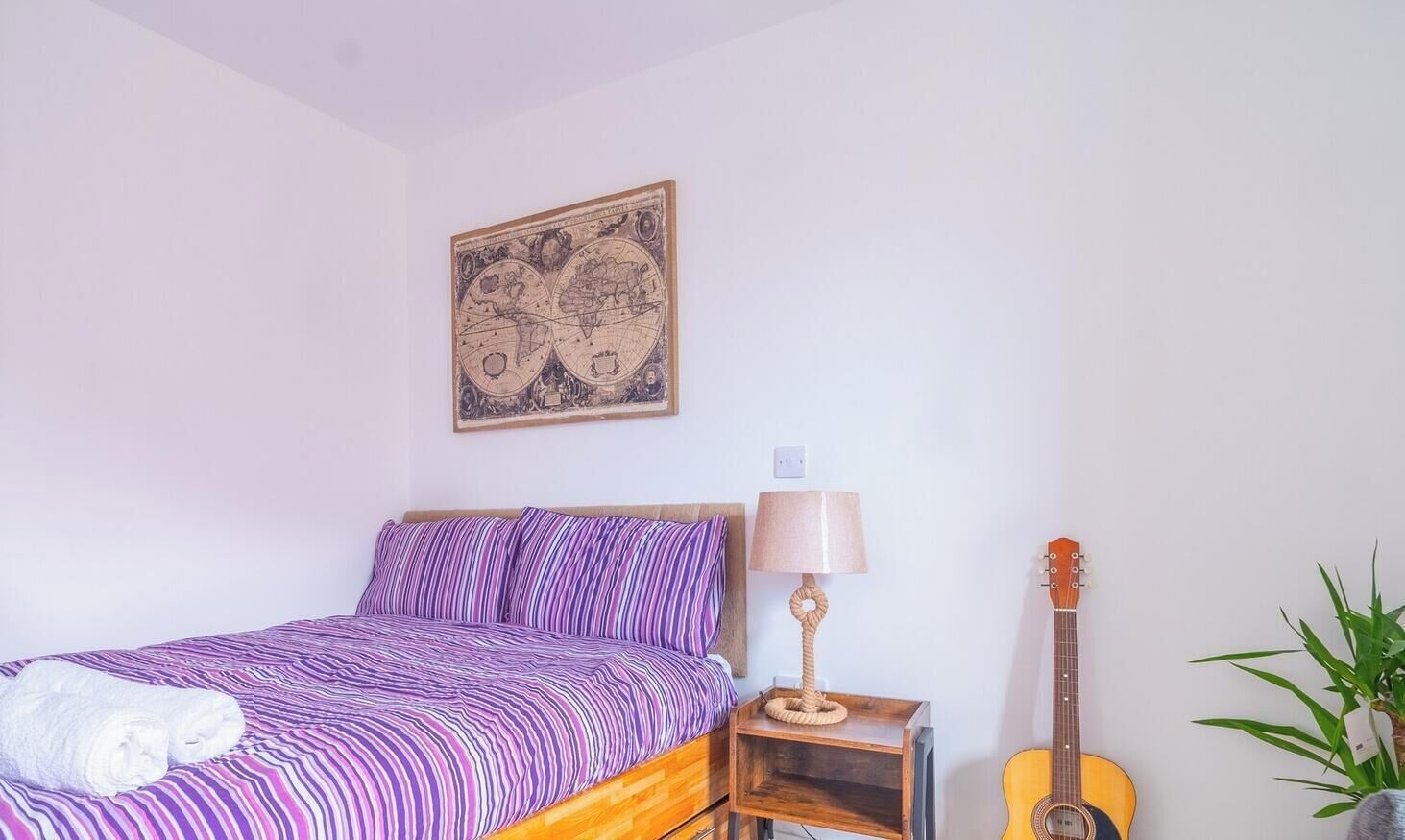 A bedroom with a bed, a guitar, a lamp, and a wall art piece.