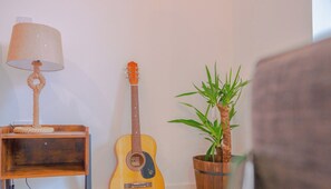 A room with a wooden nightstand, a guitar, a lamp, and a potted plant. - Creative Studio With Rustic Charm – APT 22 (Sheffield)