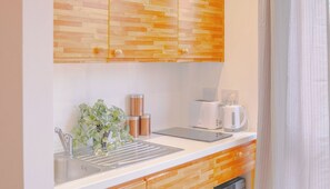 A modern kitchen with wooden cabinets, a sink, a coffee maker, and a kettle. There is a plant on the counter and a tablet. - Creative Studio With Rustic Charm – APT 22 (Sheffield)