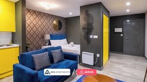 A modern apartment with a blue sofa, a bed with white bedding, a patterned wall, and a yellow kitchen. - The Noir Apartment Sheffield – APT 12 (South Yorkshire)