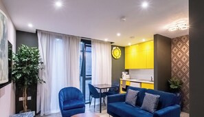 Un espace de vie compact comprenant un coin repas, une kitchenette et une grande fenêtre avec des rideaux.