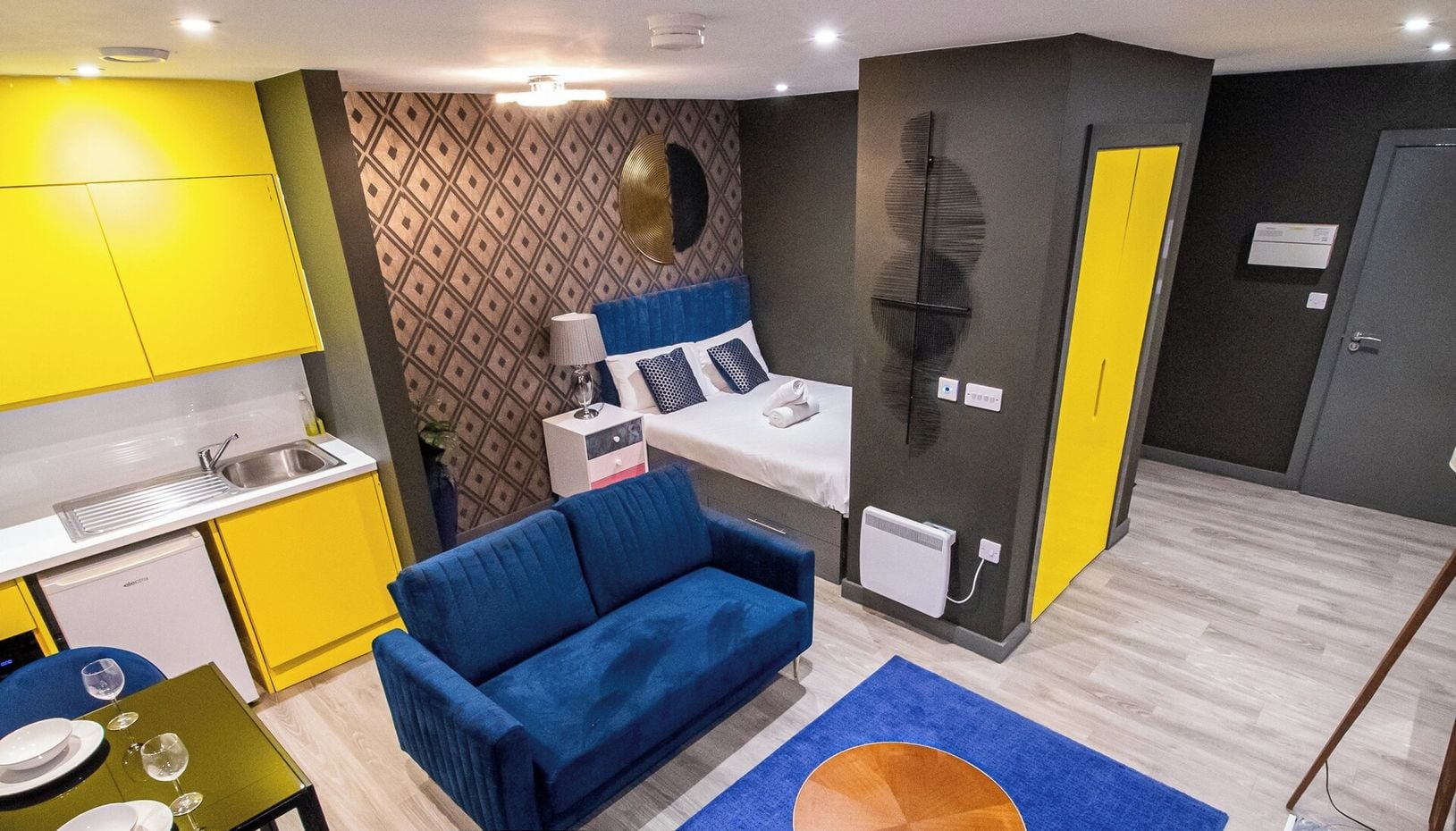 Un estudio compacto con kitchenette, cama, sofá azul y comedor.
