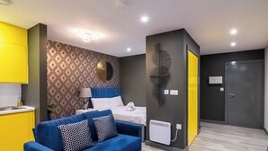 A modern apartment with a blue sofa, a bed with white bedding, a patterned wall, and a yellow kitchen. - The Noir Apartment Sheffield – APT 12 (South Yorkshire)
