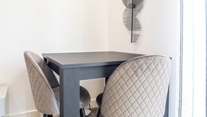 A dining area with a dark table and quilted chairs, a decorative wall piece, and logos for AVO APARTMENTS and Airbnb.