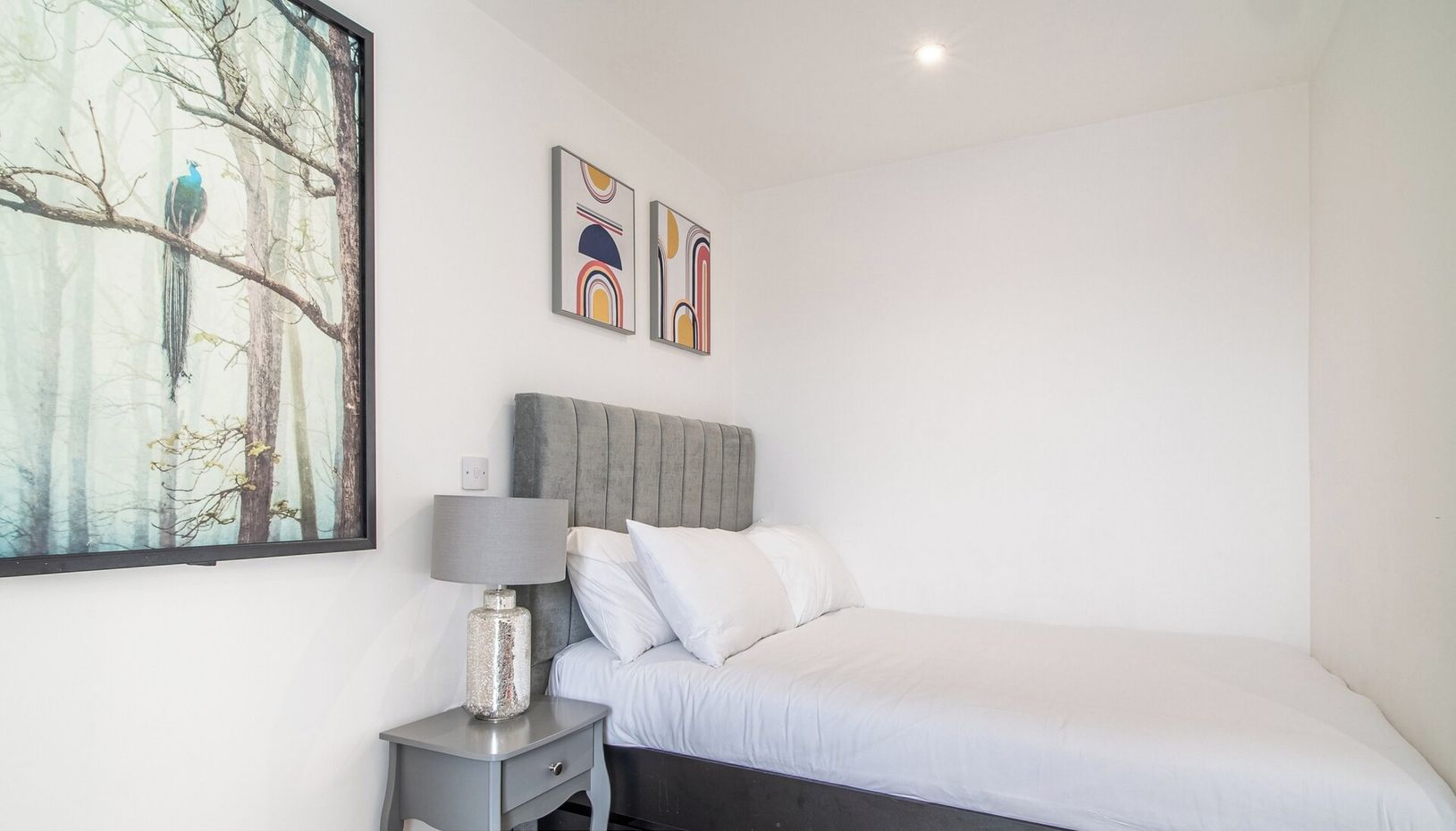 A bedroom with a bed, a nightstand, a lamp, and two abstract paintings on the wall.