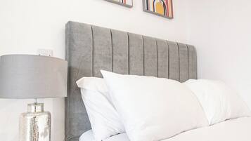 A neatly made bed with a grey upholstered headboard, white pillows, and a metallic lamp on a bedside table.