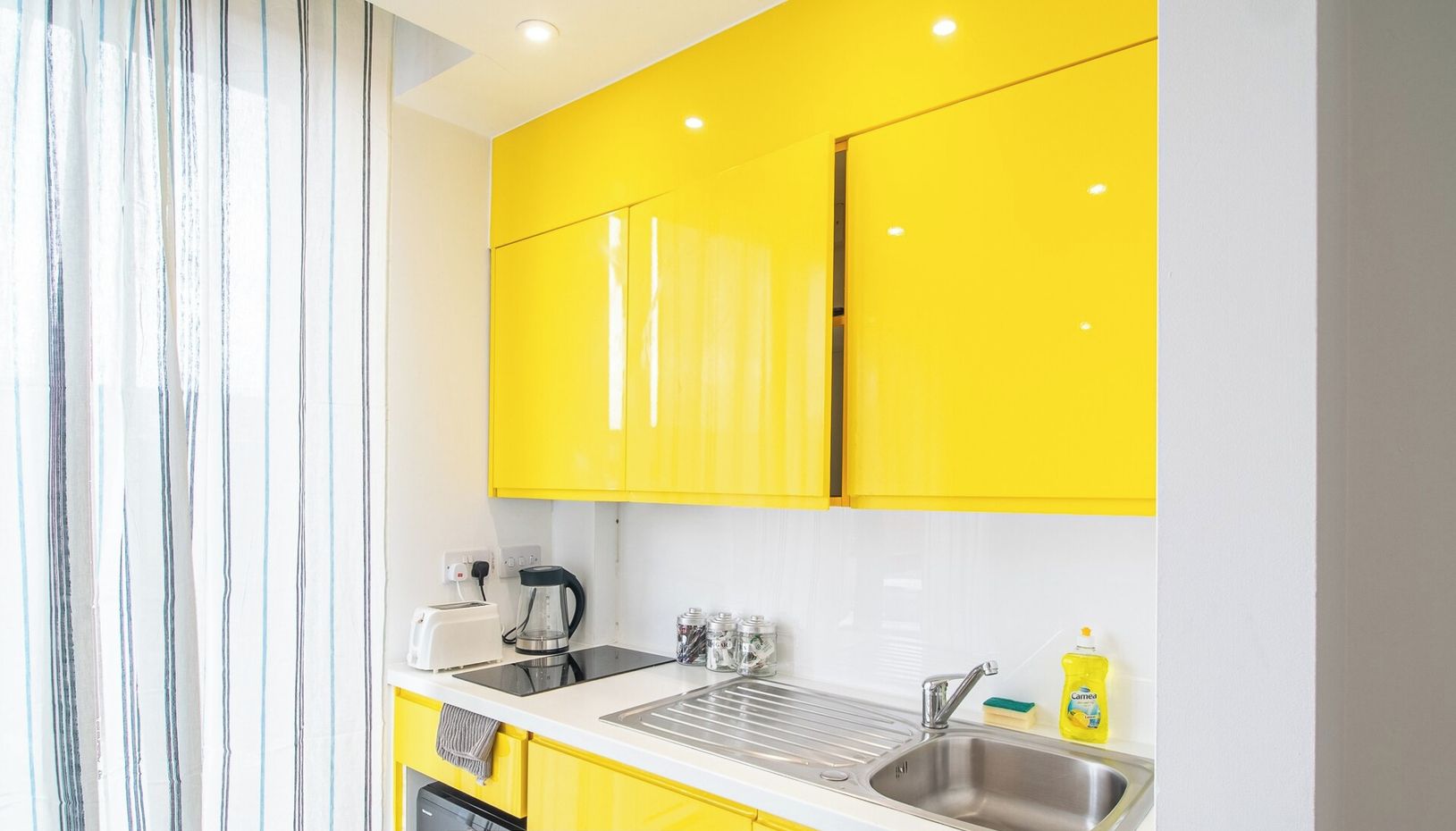 A modern kitchen with yellow cabinets, a sink, a kettle, and a toaster.