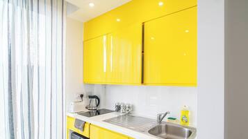 A modern kitchen with yellow cabinets, a sink, a kettle, and a toaster.