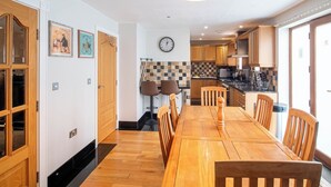 A dining area with a wooden table and chairs, a clock on the wall, and a kitchen in the background. - Luxurious Sheffield Villa 3bed with Stunning Views (Sheffield)