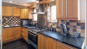 A modern kitchen with wooden cabinets, a gas stove, an oven, and a tiled backsplash. - Luxurious Sheffield Villa 3bed with Stunning Views (Sheffield)