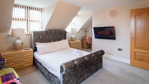 A bedroom with a bed, a TV, a lamp, a dresser, and a window with blinds. - Luxurious Sheffield Villa 3bed with Stunning Views (Sheffield)