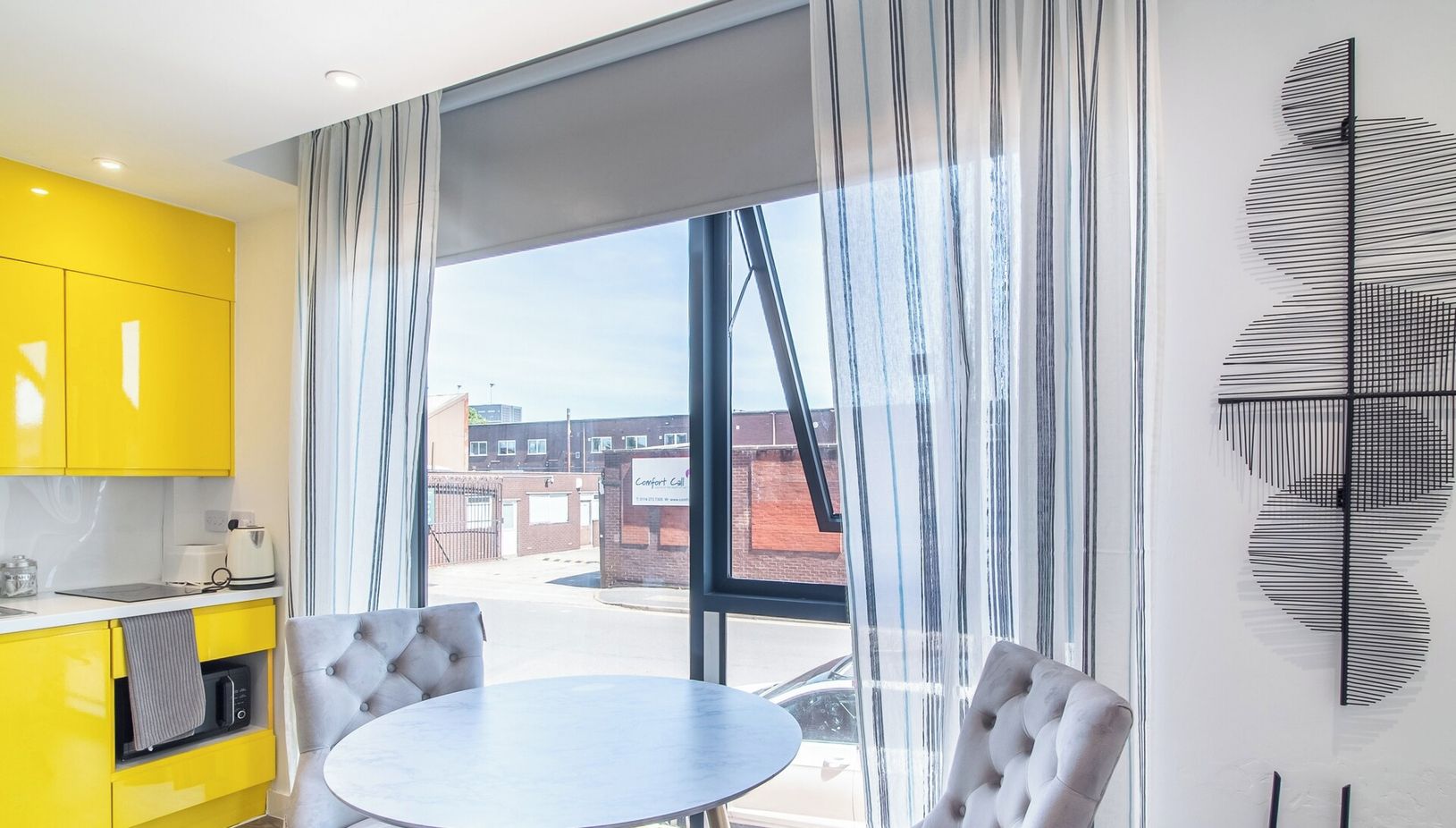 A modern apartment with a dining area, kitchen, and large windows offering a city view.