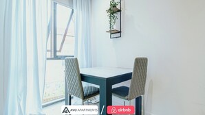 A modern dining area with a table and two chairs, a window with curtains, and a wall-mounted plant. - Modern Sheffield Studio With WiFi – APT 15 (Sheffield)